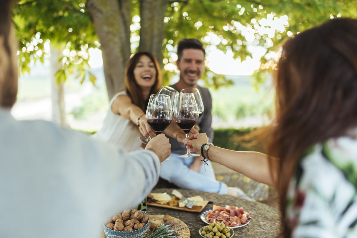 Una pareja sentada en una mesa con comida y brindando con otra pareja con vino tinto.